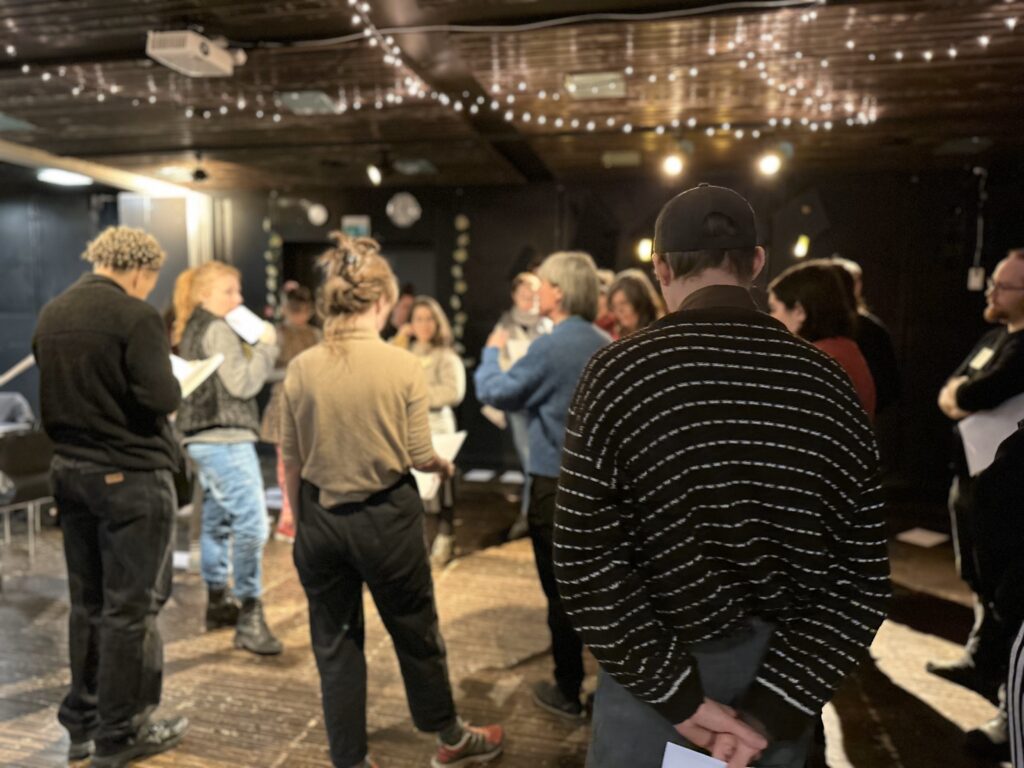 Group stand in the studio during a workshop. There are fairy lights above them.